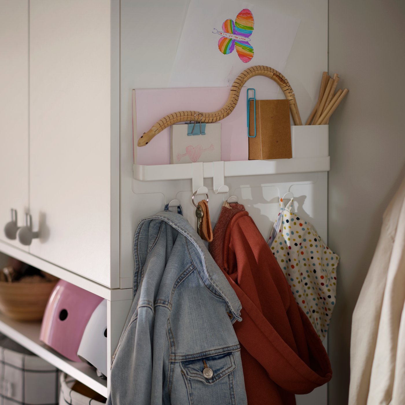 Ett hörn i en hall med en ALTARLIDEN kroklist med förvaring som håller jackor, väskor och småsaker på sidan av en garderob.