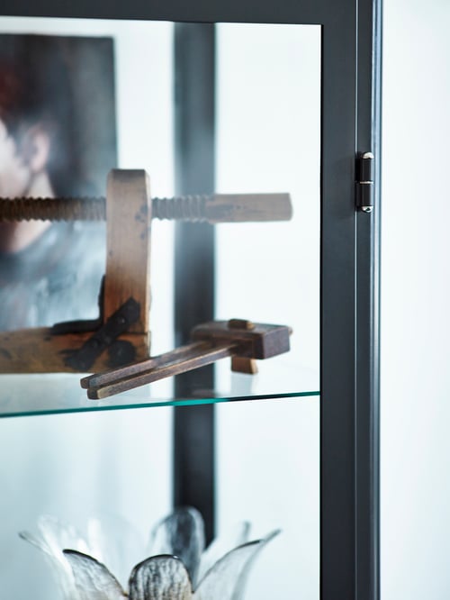 Wohnzimmer mit weißer Wand mit Nahaufnahme des Glasbodens einer Vitrine, auf dem zwei Holzgegenstände stehen.