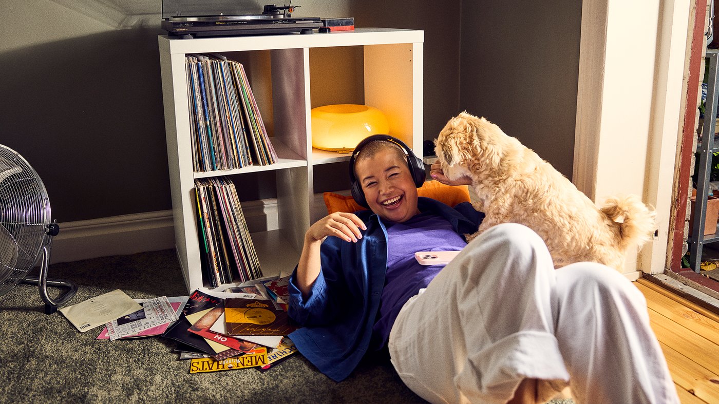 A lady sitting on the floor whilst playing with her dog, next to a white KALLAX shelving unit. 