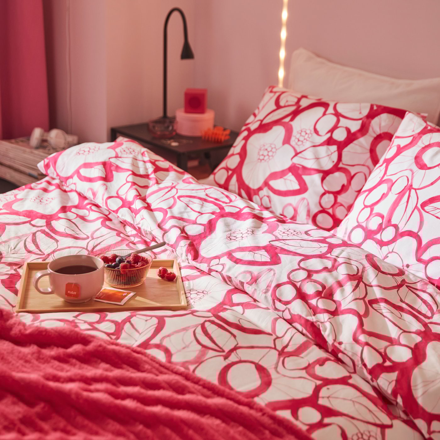 A bed with a white and bright pink floral HÄRLIR duvet cover and pillowcase and a bright pink GULLSTRÅLE bedspread.