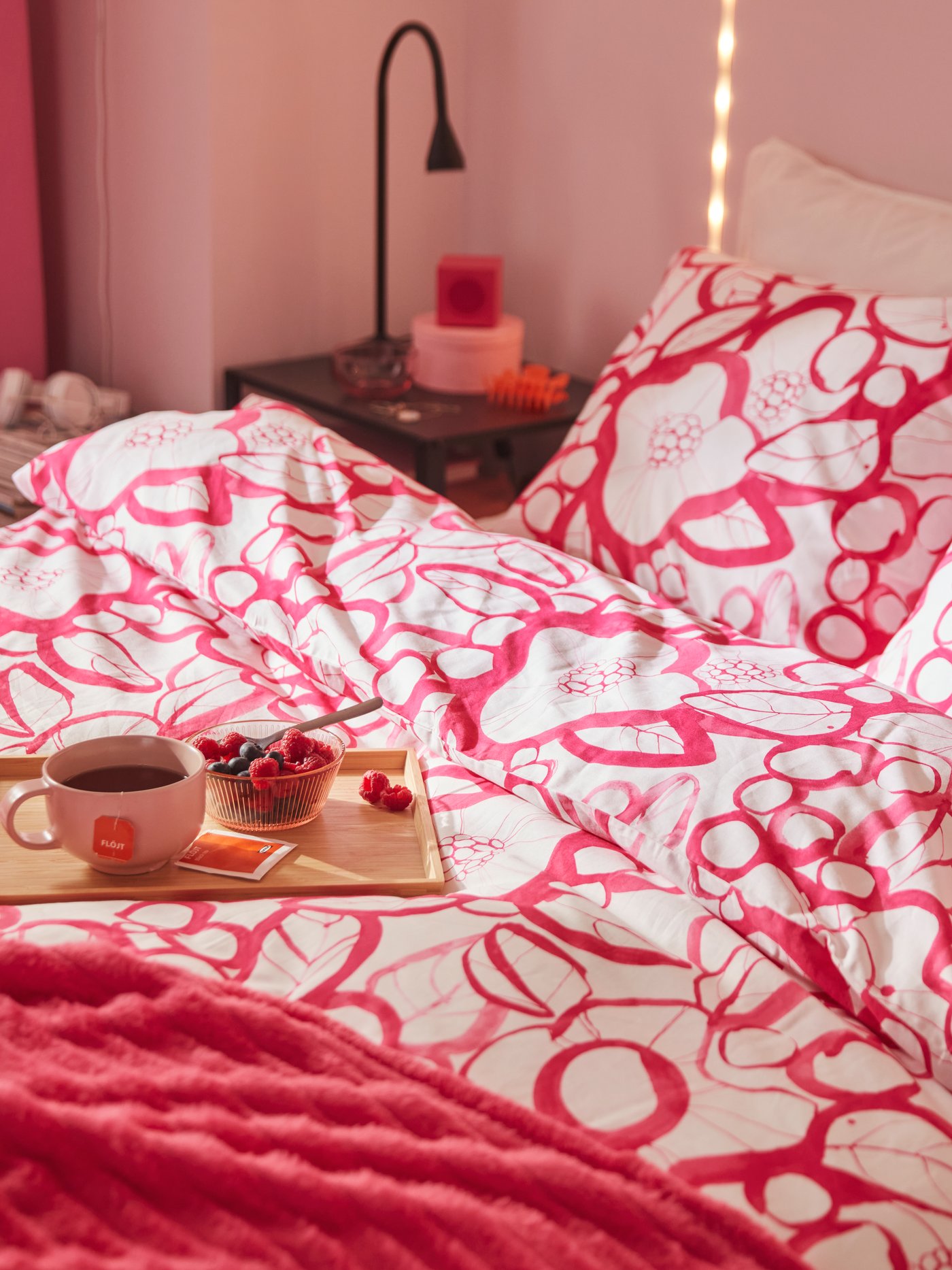 A bed with a white and bright pink floral HÄRLIR duvet cover and pillowcase and a bright pink GULLSTRÅLE bedspread.