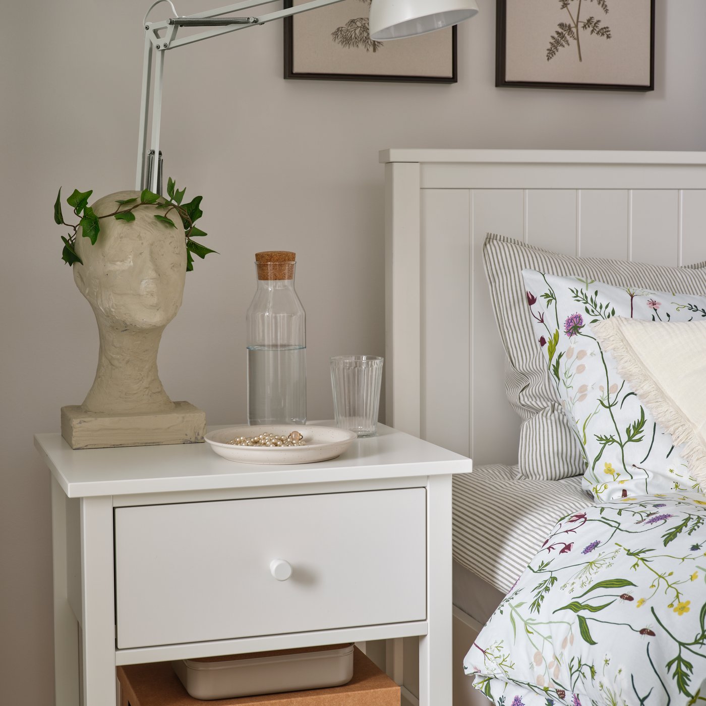 A bedroom with a white GULLABERG bedside table featuring a drawer and a shelf next to a white GULLABERG bed with pillows.