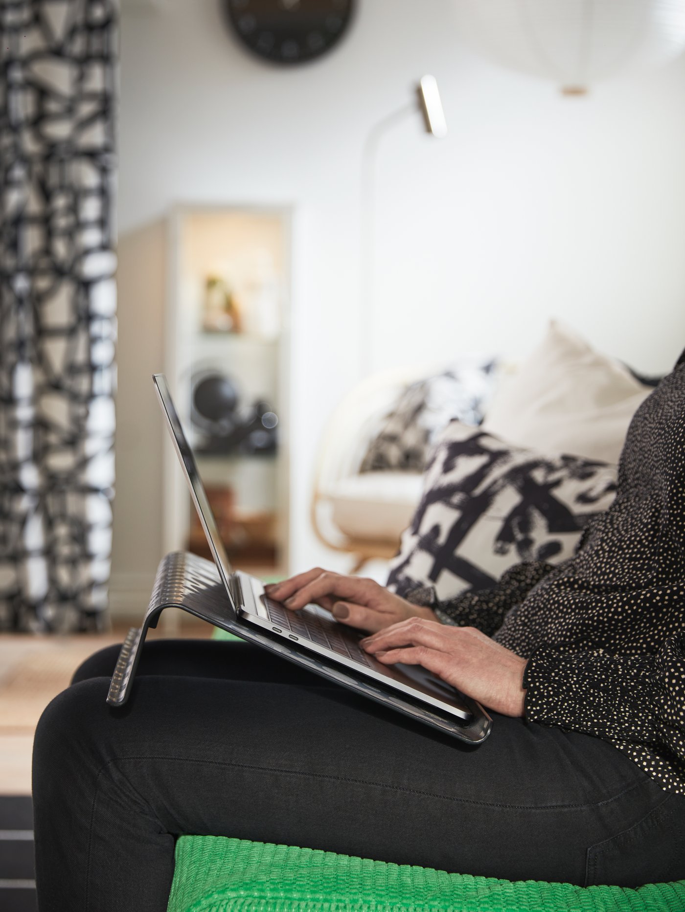 A person sitting on a Vansbro bright green 2-seat sofa-bed with a black laptop support and laptop.