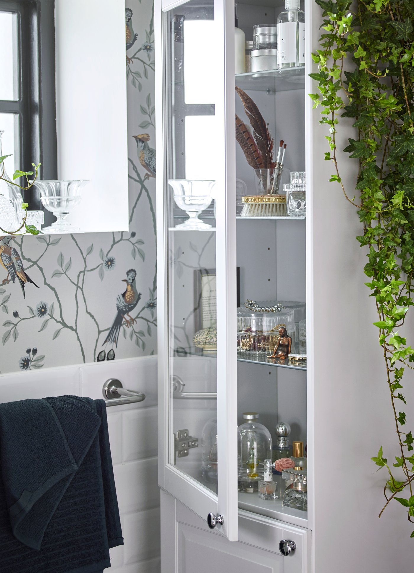 Jasnoszara wysoka szafka IKEA GODMORGON ma pełne drzwi na dole i drzwi z bezbarwnego szkła na górze oraz szklane półki wewnątrz, które pozwolą wyeksponować ukochane przedmioty, chroniąc je jednocześnie przed wilgocią. Pudełka z bezbarwnego szkła SAMMANHANG z korkowymi pokrywkami to miły dodatek do przechowywania łazienkowych przyborów i biżuterii. 