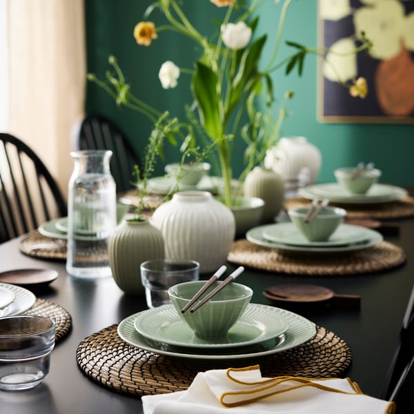 A dining table is set with pale grey-green STRIMMIG bowls,  plates and side plates, chopsticks, glasses and flowers.