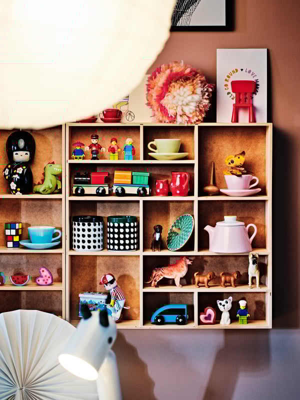 Two birch plywood SKUTSKÄR display shelves on a wall displaying an assortment of toys including a DUKTIG 3-piece tea playset.