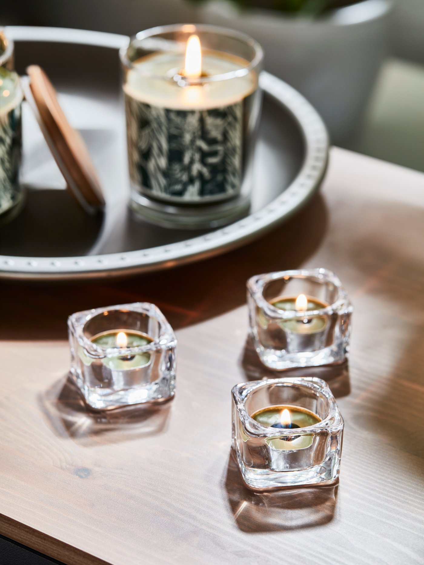 Duftkerzen auf einem Tablett und daneben Teelichthalter aus Glas auf einem Tisch. 