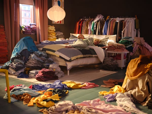 chambre mal rangée avec des vêtements sur le lit et sur le sol