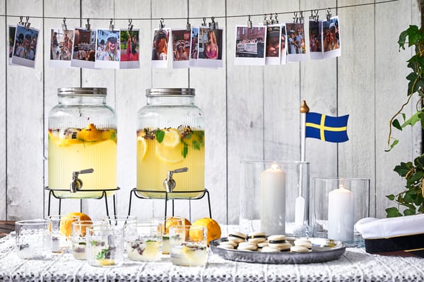 Ett festligt bord dukat för en svensk studentmottagning med två stora lemonadbehållare, glas, macarons, en svensk flagga och en studentmössa.