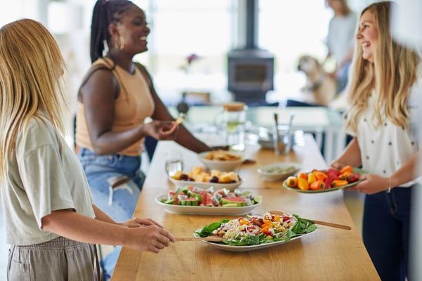 A group of colleagues sit around a table sharing a potluck lunch. 