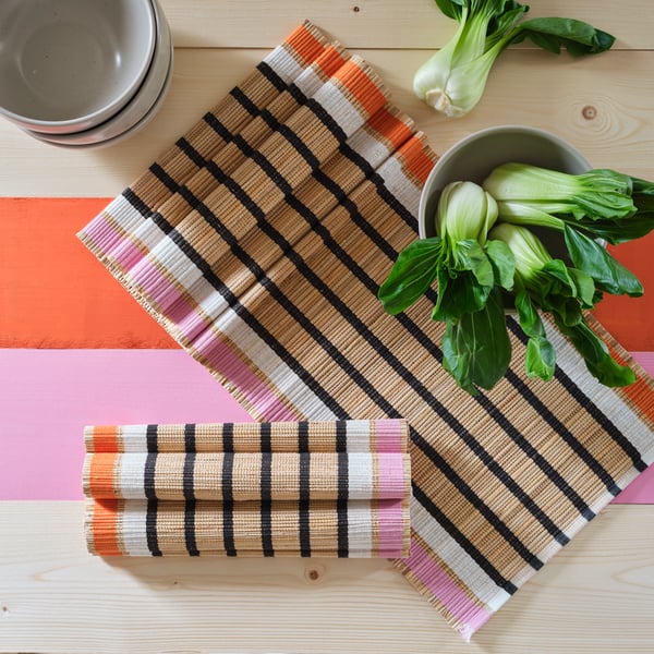 Two MÄVINN table-runners lie on a painted wooden table. The table also holds ceramic bowls and green vegetables.