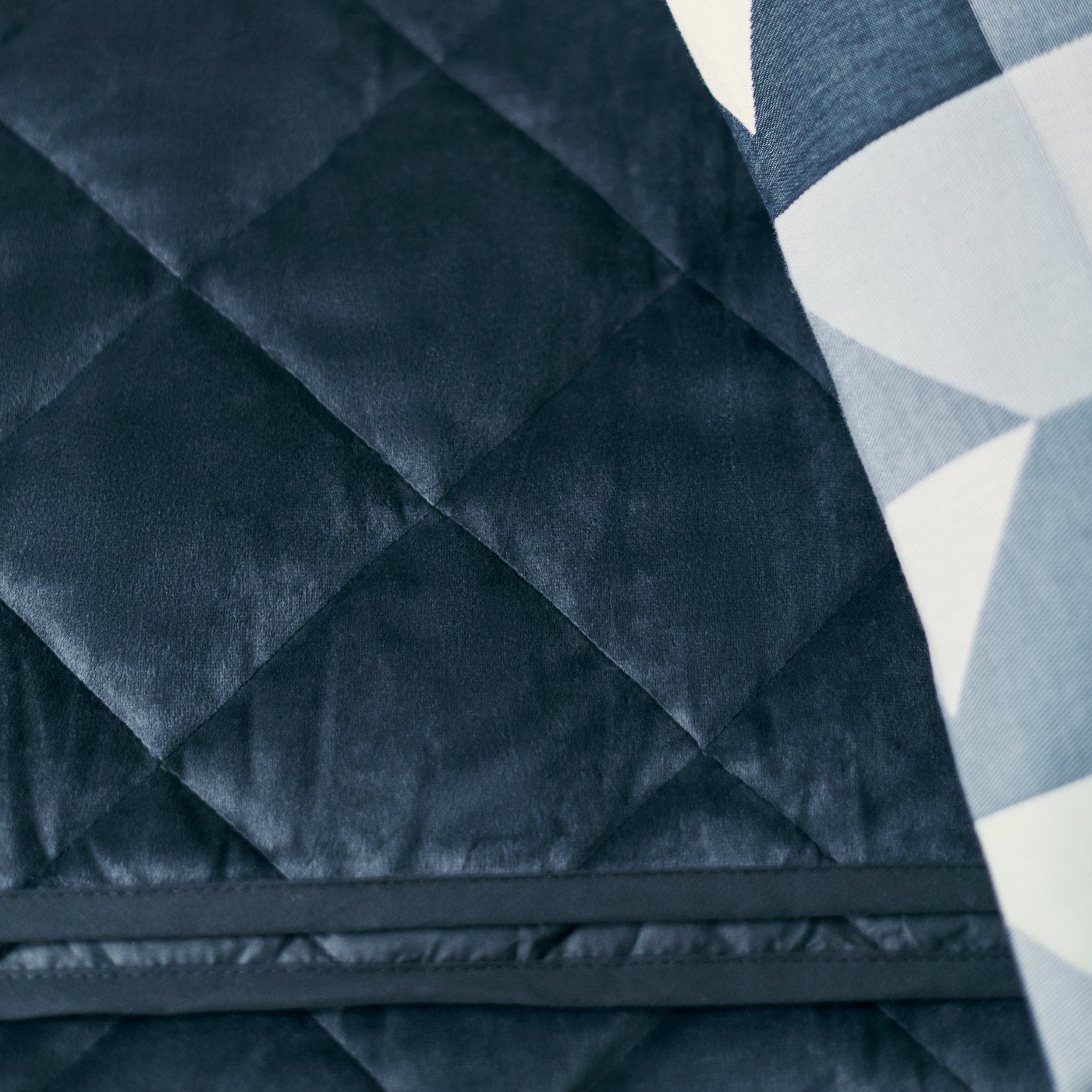 A dark grey MJUKPLISTER quilted bedspread beside a cushion covered in a blue/green SVARTHÖ cover.