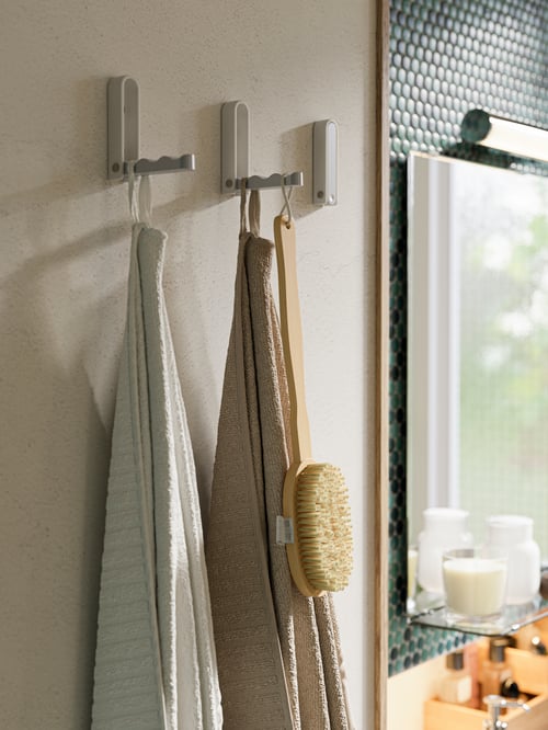 Dans la salle de bains, plusieurs crochets pliants gris en aluminium et en acier inoxydable soutiennent deux serviettes de bain éponge.