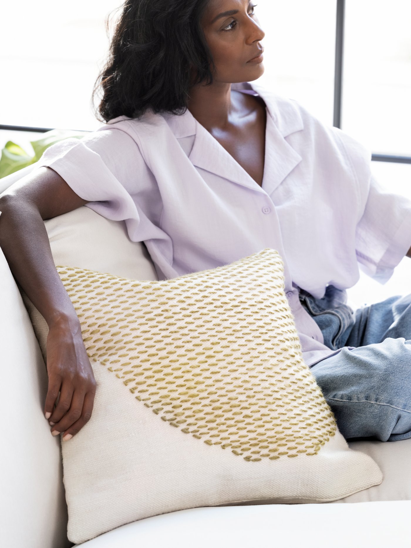 A woman is sitting in a sofa with a LOKALT cushion, handmade by Indian artisans and inspired by traditional embroidery.