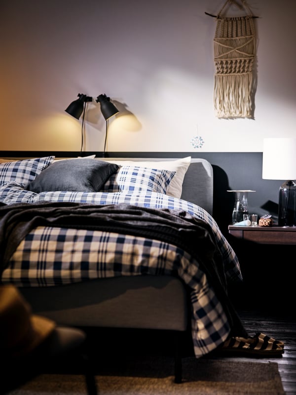 A light-grey SLATTUM upholstered bed made with SPIKVALLMO bed linen and lit by double, dark-grey HEKTAR spotlights.