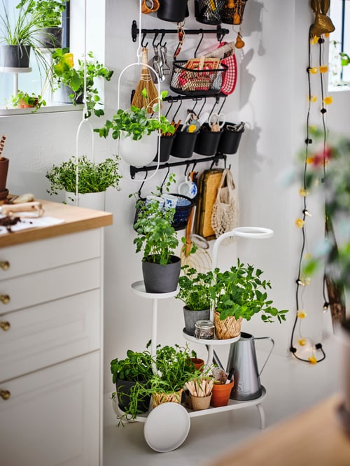 O bucătărie cu șine HULTARP cu containere negre umplute cu accesorii pentru bucătărie și un suport pentru plante cu roți sub ele.