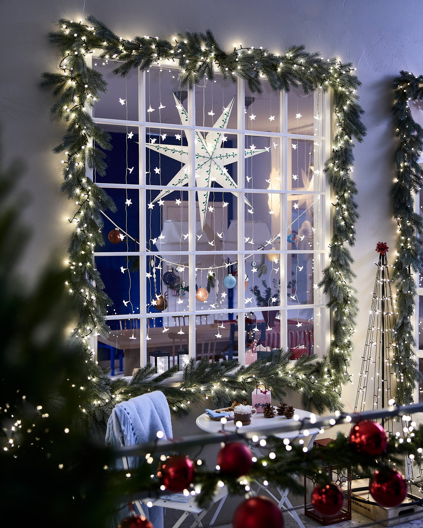 Ett stort fönster med grangirlanger och ljusslingor. En adventsstjärna hänger i mitten.