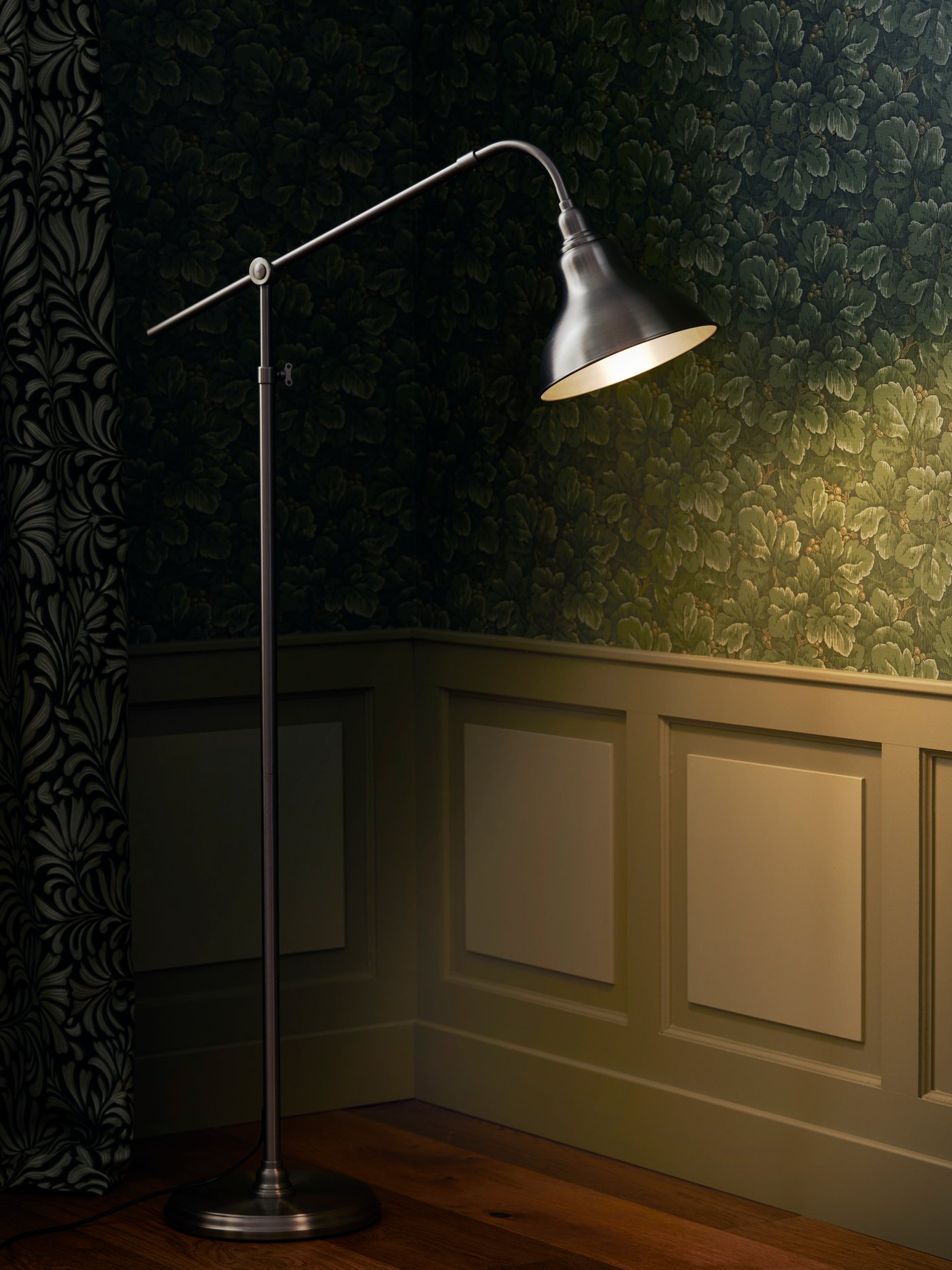 Detalle de una lámpara de lectura de pie hecha de aluminio y revestimiento acrílico con cabezal y brazo regulables, en un dormitorio moderno.