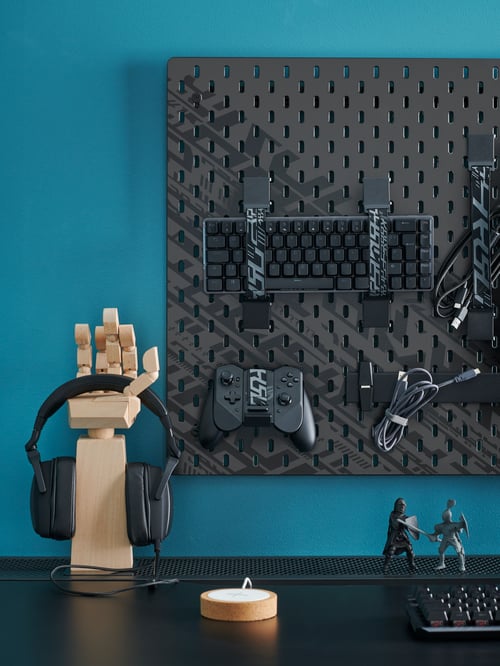 Un bureau avec des accessoires de jeu sur un panneau perforé UPPSPEL noir et un casque d’écoute sur un support à accessoires LÅNESPELARE.