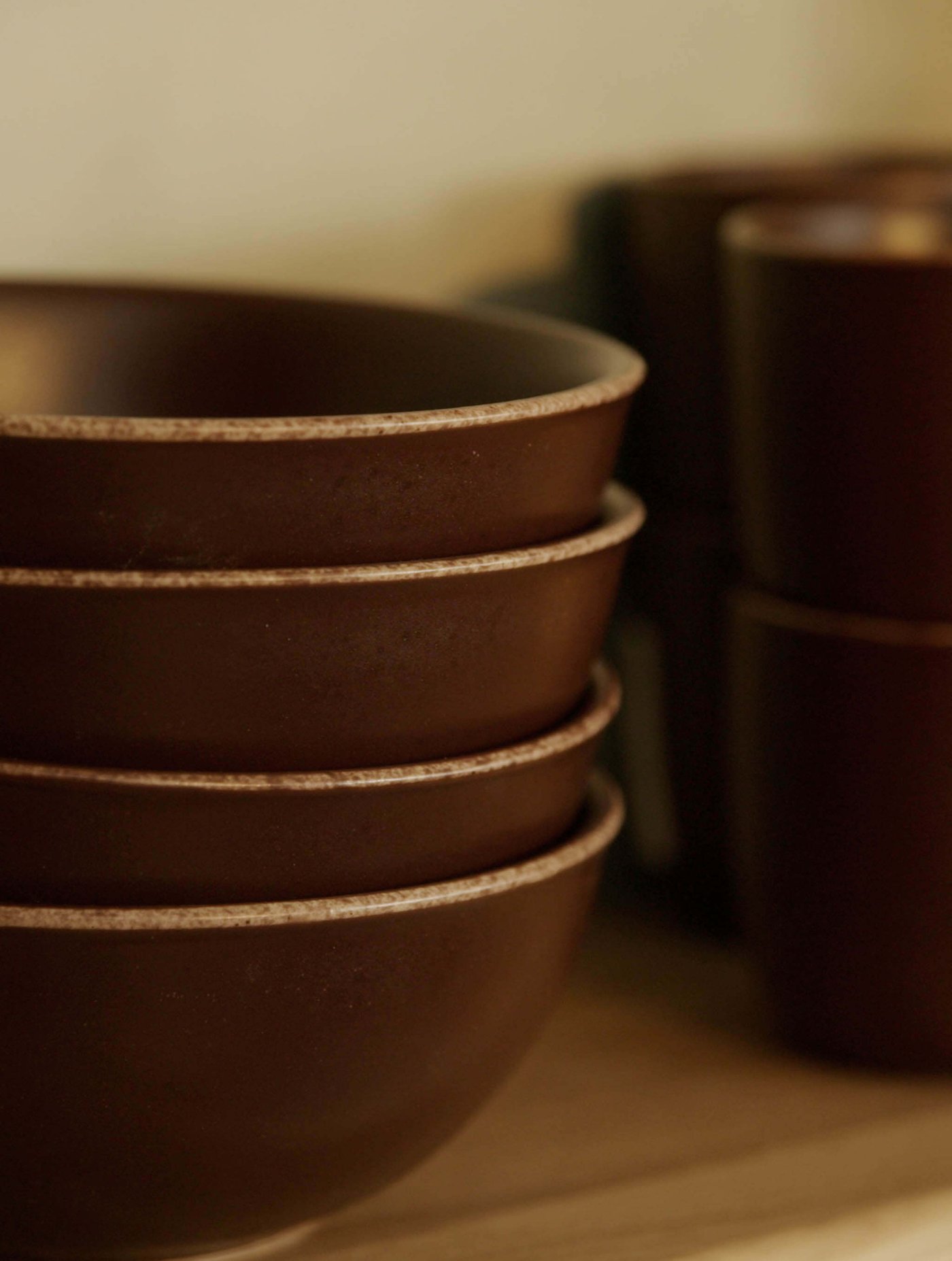Stack of dark ceramic bowls on a wooden shelf.