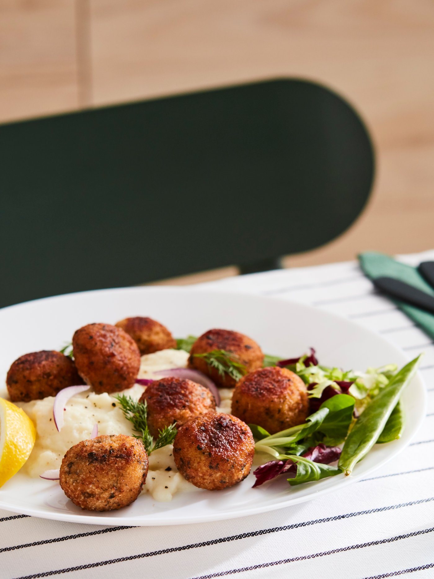 Salmon and cod balls on a white plate with mashed potatoes and salad, on a table dressed in blue and white tablecloth.