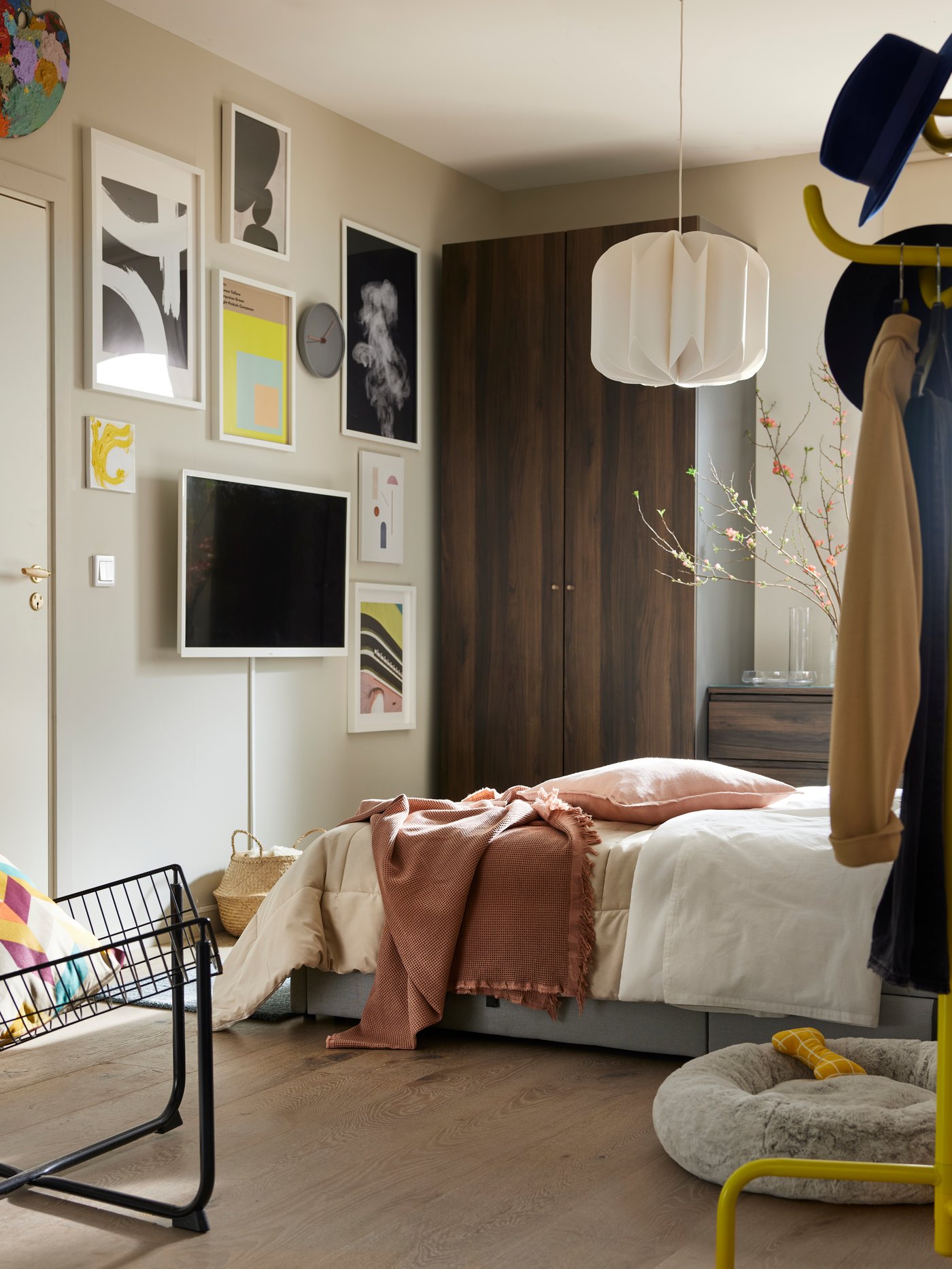 En grå GLADSTAD seng med grønne og cremefarvede tekstiler på, og som står foran et PAX/STORKLINTA garderobeskab og over for en væg fuld af billeder.