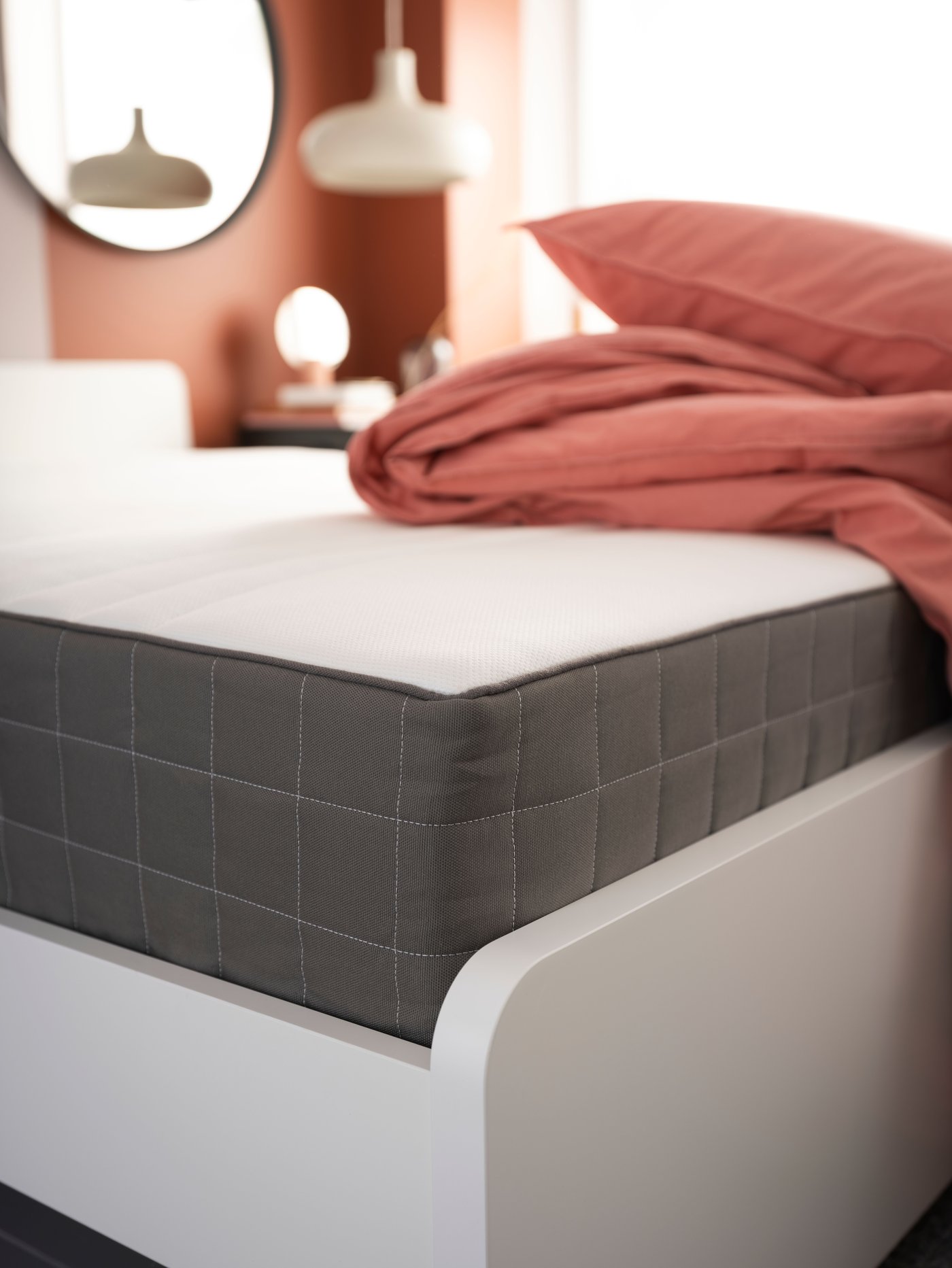 Un matelas à ressorts HAUGESUND sur une structure de lit blanche avec une housse de couette et un oreiller empilés dessus.