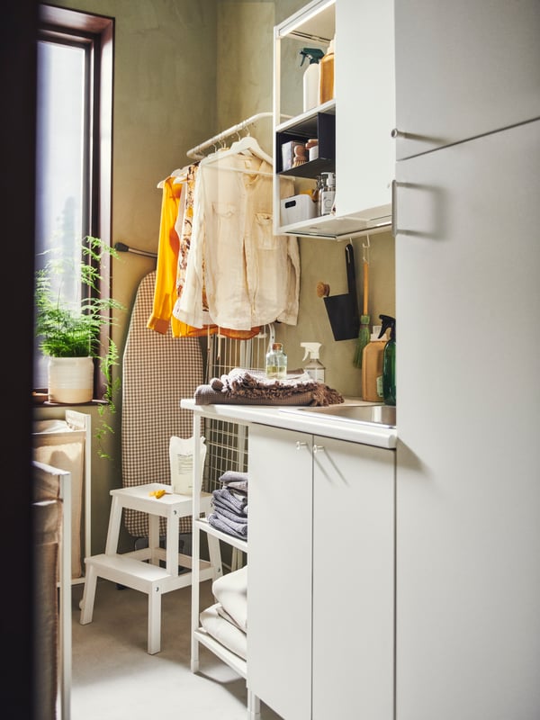 A BEKVÄM step stool is on the floor underneath a mounted clothing rail. An ENHET laundry combination is next to it.