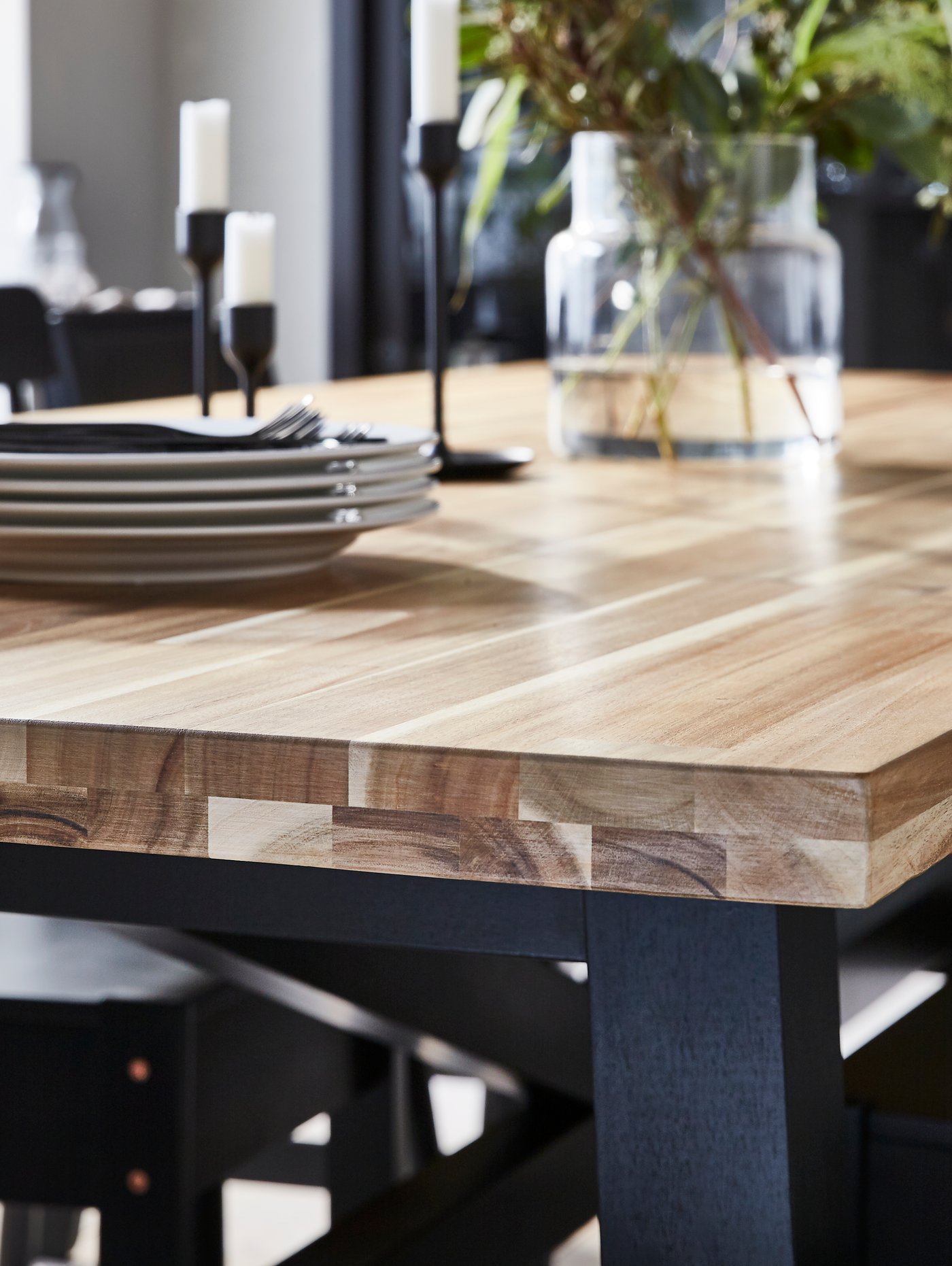 Une table à manger avec un dessus en bois doté d’un joli grain sur laquelle se trouvent une pile d’assiettes, quelques chandeliers et un vase.
