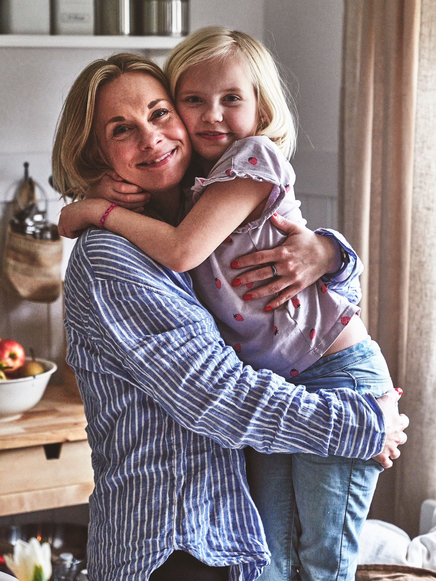 En mamma och en dotter kramas i ett kök.