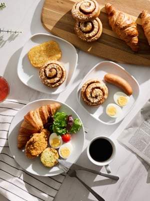 A breakfast table with three plates, coffee, and a newspaper.