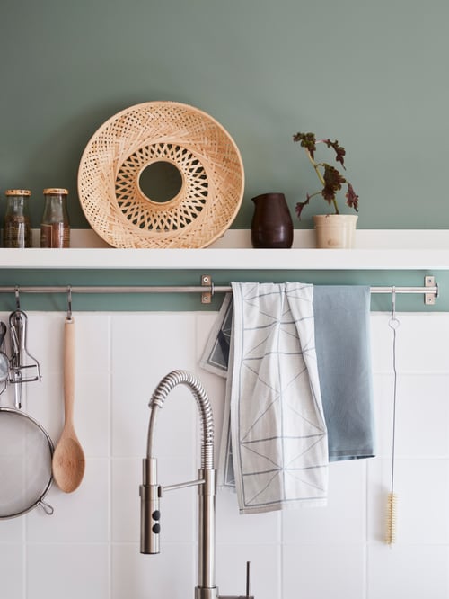 A MOSSLANDA picture ledge holding a variety of kitchen items is mounted on the wall above a VIMMERN kitchen mixing tap.