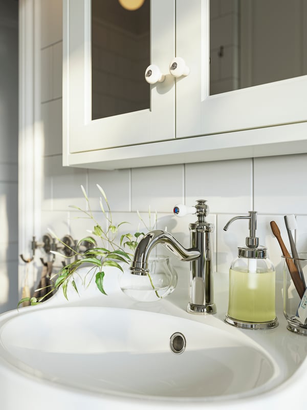 A close-up of a white TÄNNFORSEN mirror cabinet with doors over a wash-basin with a HAMNSKÄR wash-basin mixer tap.