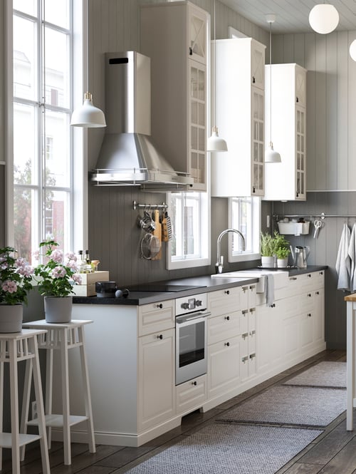 Kitchen with base cabinets with space for oven, wire basket, drawers, doors, plant stand, oven, hob, extractor hood, plants.