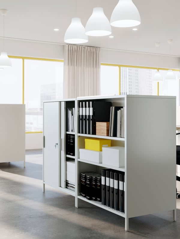 Free-standing TROTTEN storage with sliding doors and open display, shown in an office. Black binders and white boxes inside.