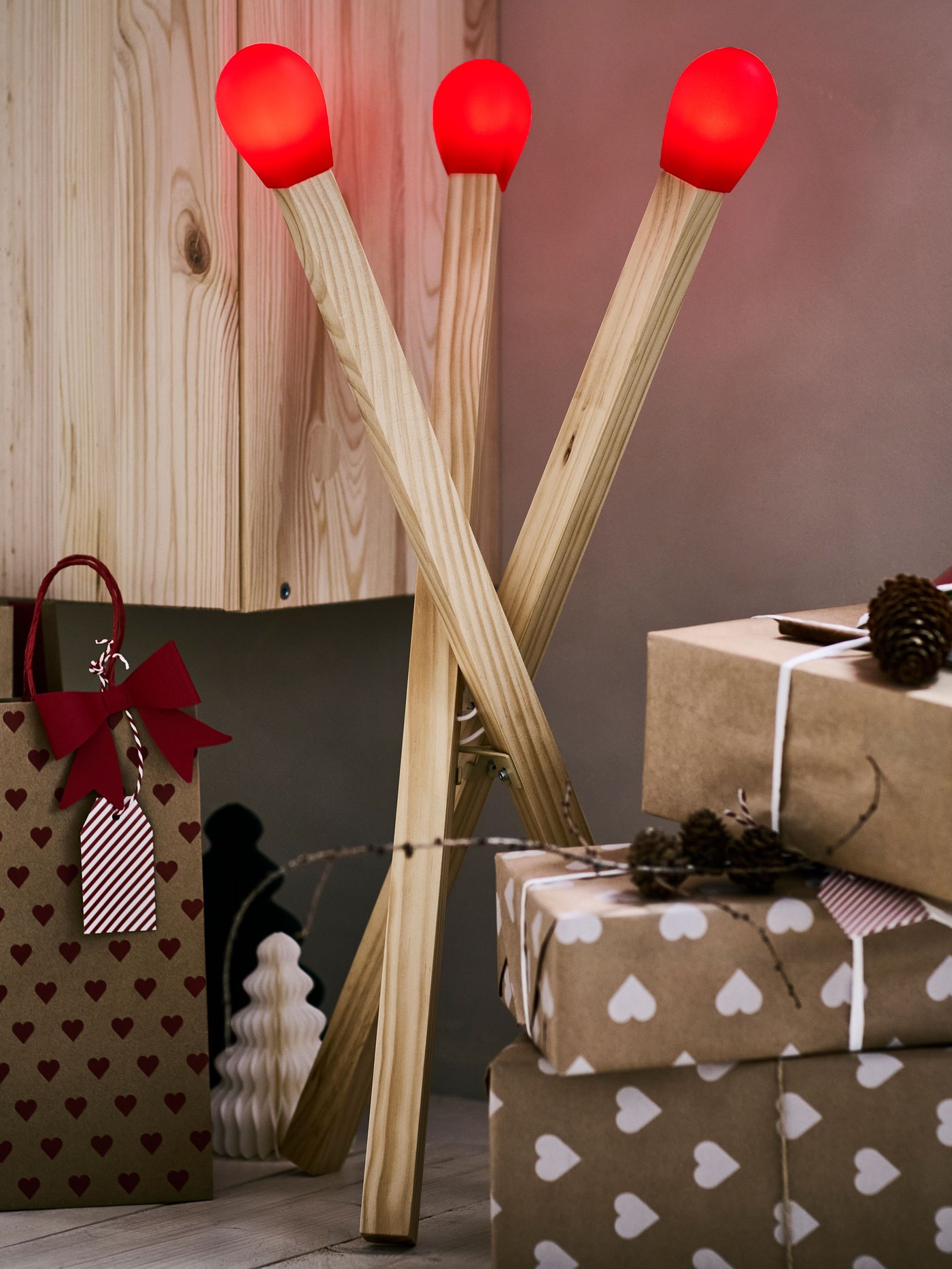 Una lampada da terra STRÅLA LED in legno a forma di fiammifero e accanto ad essa alcuni regali avvolti nella carta da regalo IKEA.