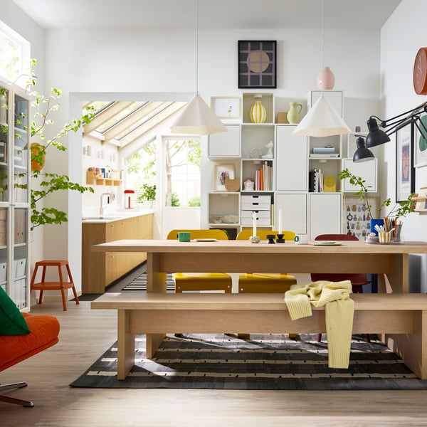 A bright dining room has a BERGSHYTTAN table with a bench in birch veneer on one side and colourful chairs on the other.