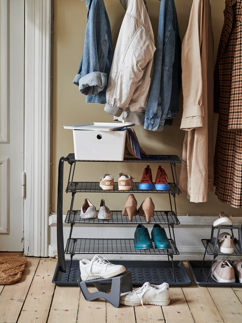 A wooden-floor hallway with a row of hanging garments above stacked GREJIG shoe rack and a single MURVEL shoe organiser.