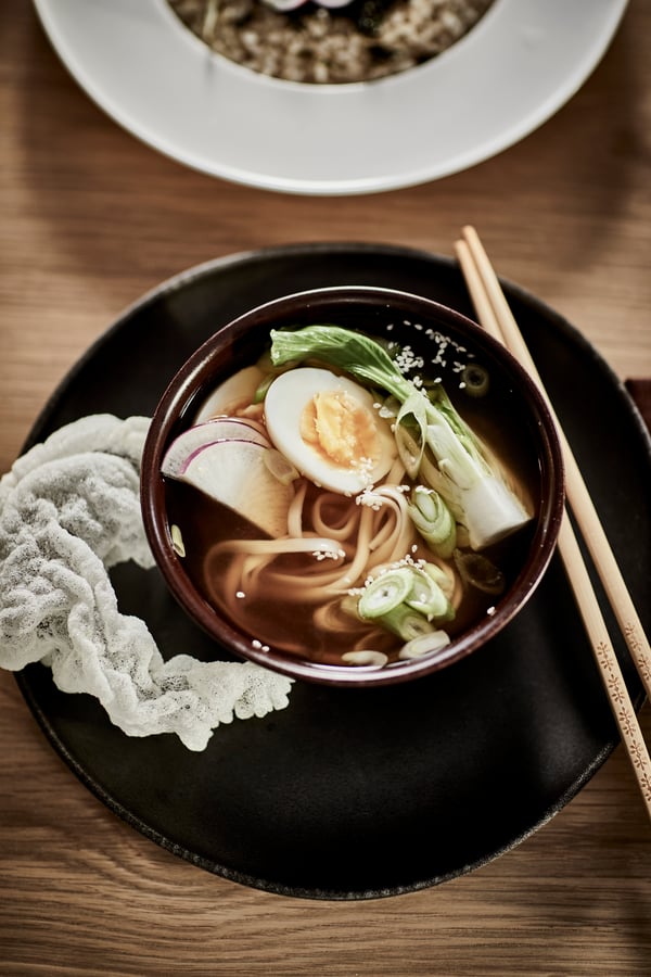 En brun STOCKHOLM 2025 skål med ramen suppe i og spisepinde ved siden af.