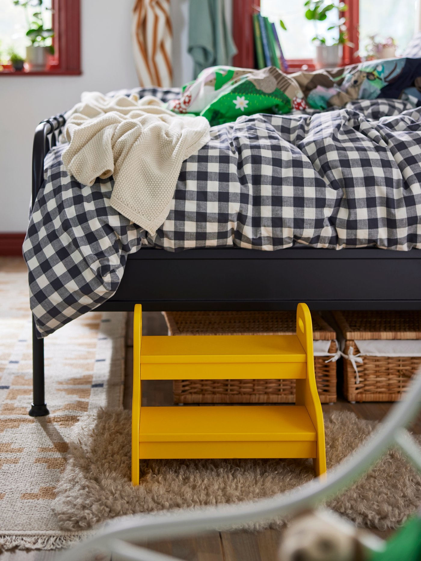 Close-up on bed with EKTANDVINGE check pattern duvet cover, and a yellow TROGEN children’s step stool standing next to it.