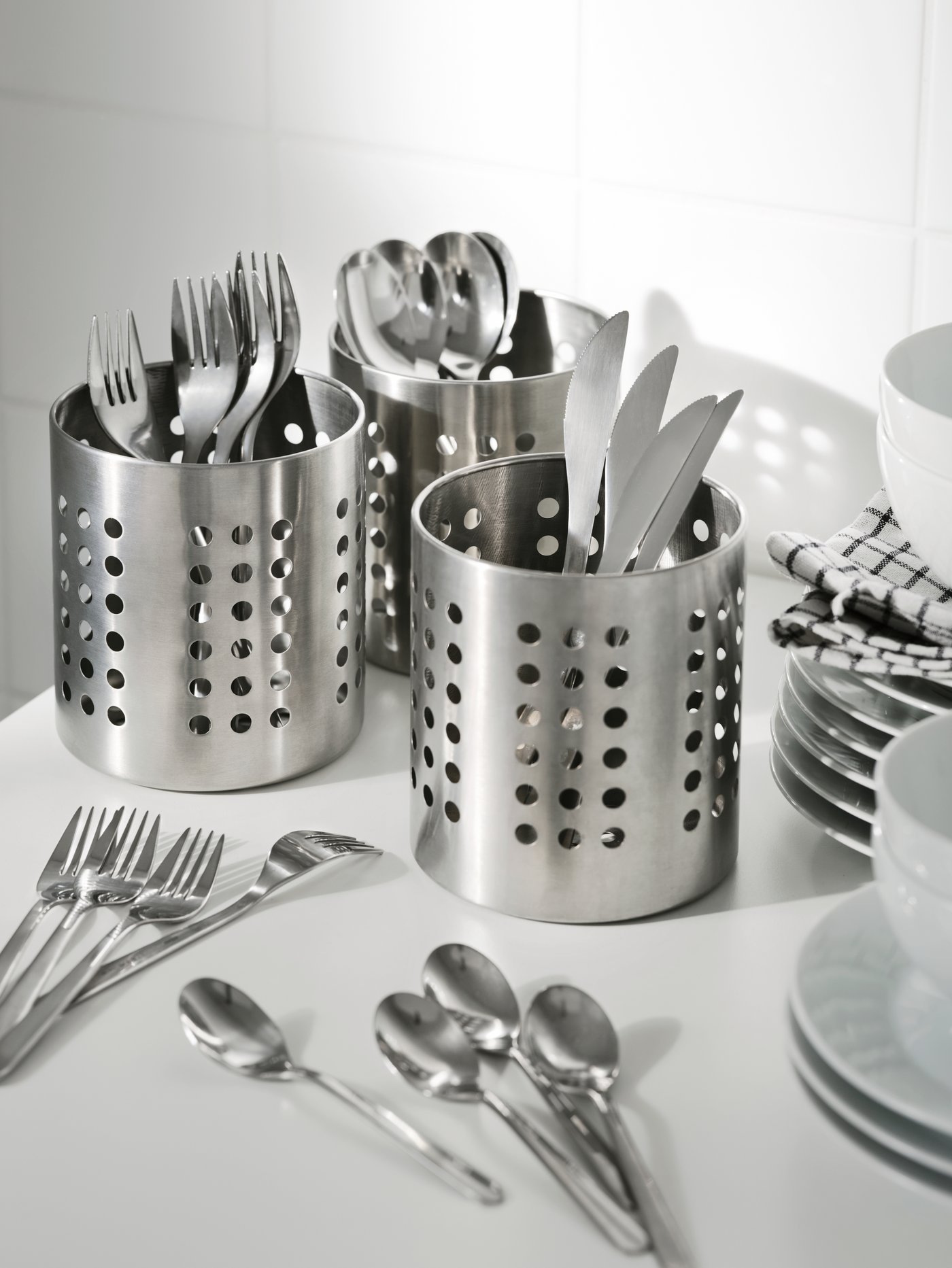 Cocina moderna con una cubertería de 24 piezas separada en tres soportes para cubiertos junto a tazas y platos.