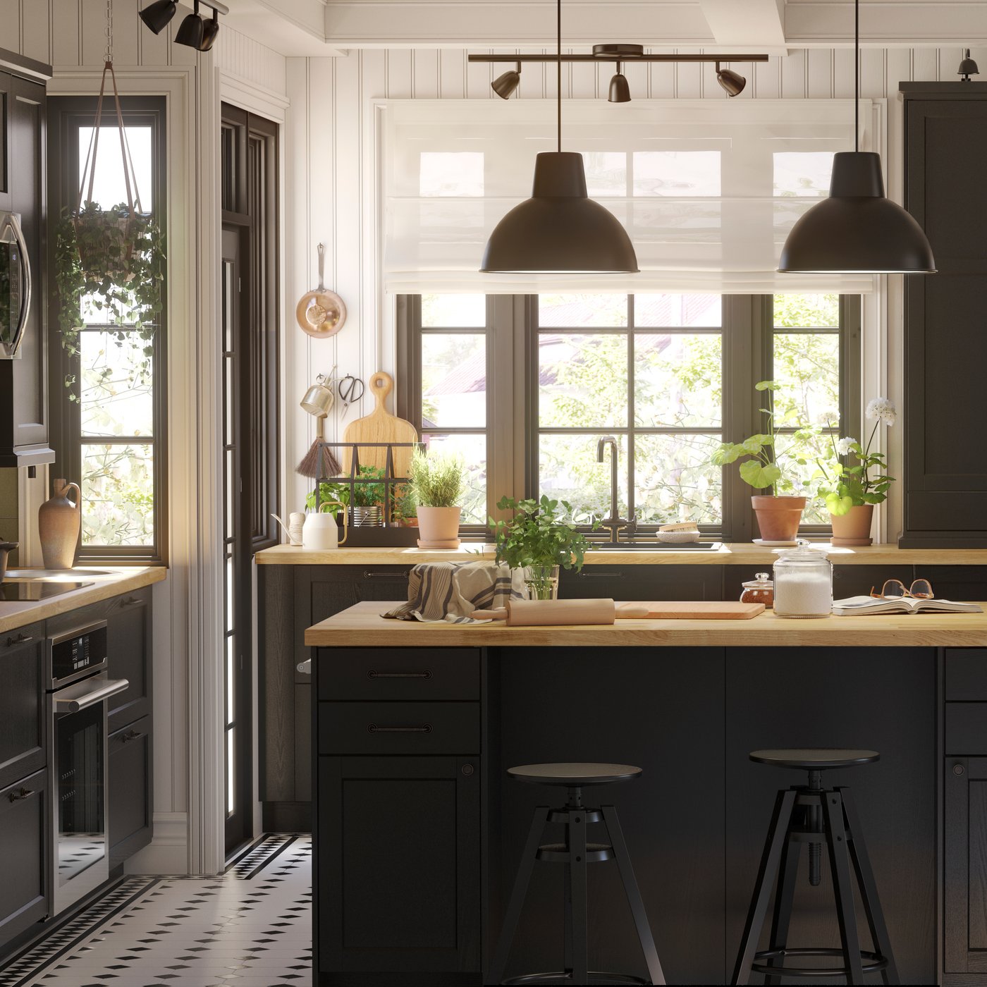 ห้องครัวขนาดใหญ่ที่มีบานตู้ LERHYTTAN/เลียร์ฮึตตัน ย้อมสีดำและท็อปเคาน์เตอร์ไม้มาพร้อมโต๊ะเตรียมอาหารและโคมไฟแขวนเพดานสีดำ 2 ดวง