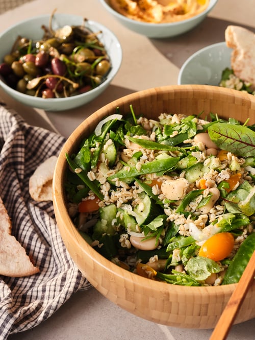 Tischplatte mit einer BLANDA MATT Servierschüssel aus Bambus, in der Salat angerichtet ist. Daneben liegt ein Geschirrtuch.