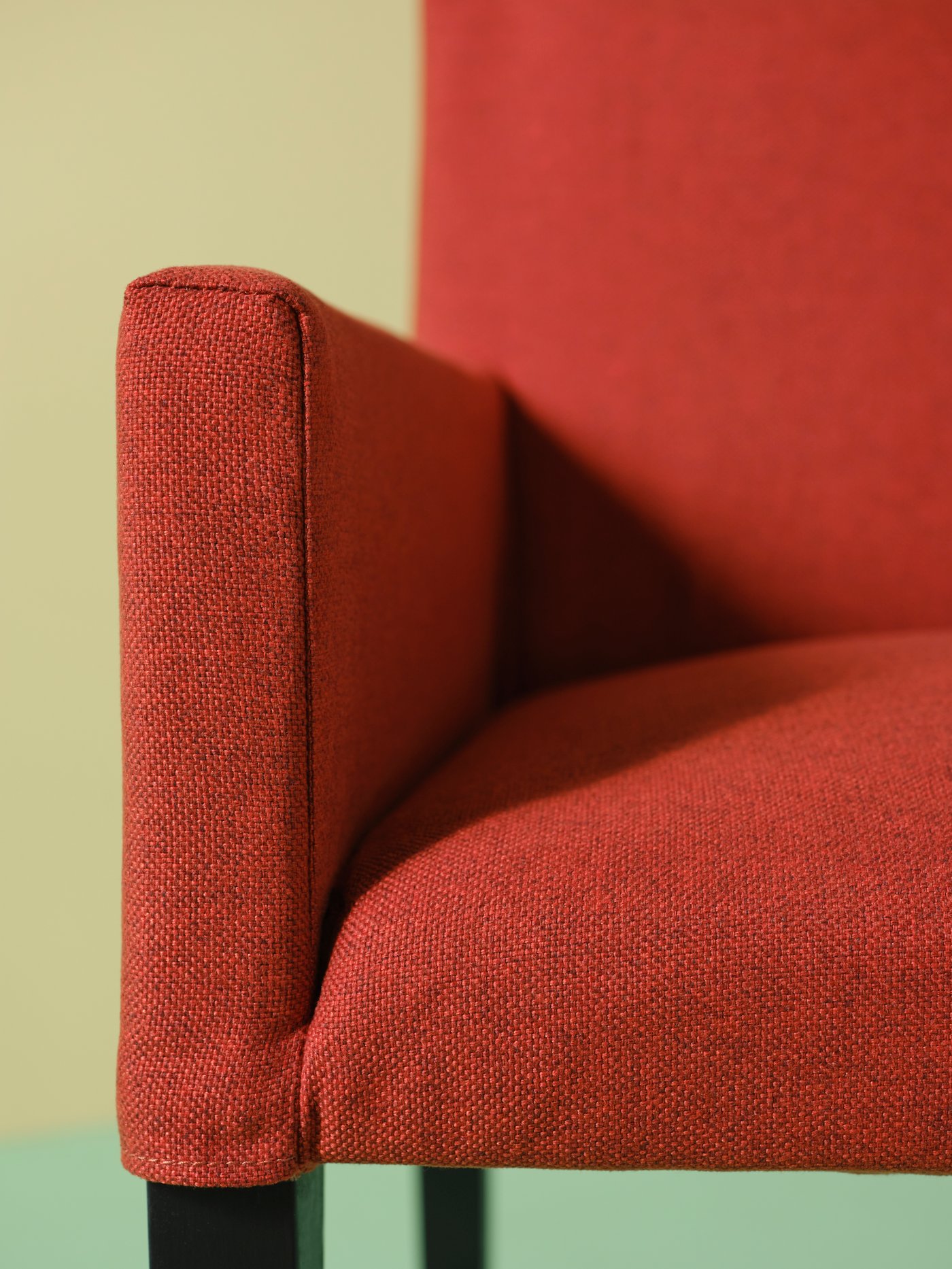 Primer plano de la esquina de un salón con una silla MÅRENÄS roja con reposabrazos de madera maciza y una funda de poliéster.