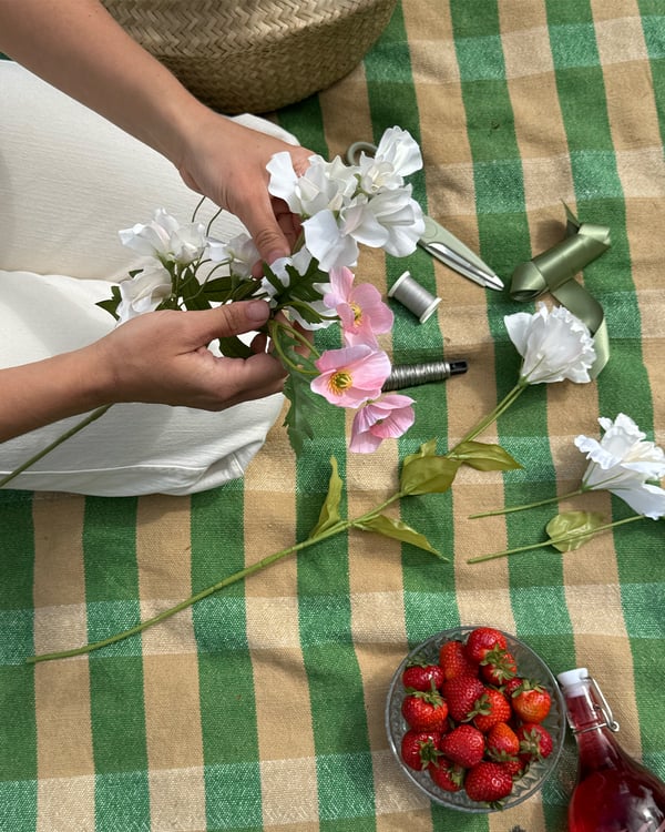 En person binder små blombuketter till en midsommarkrans.