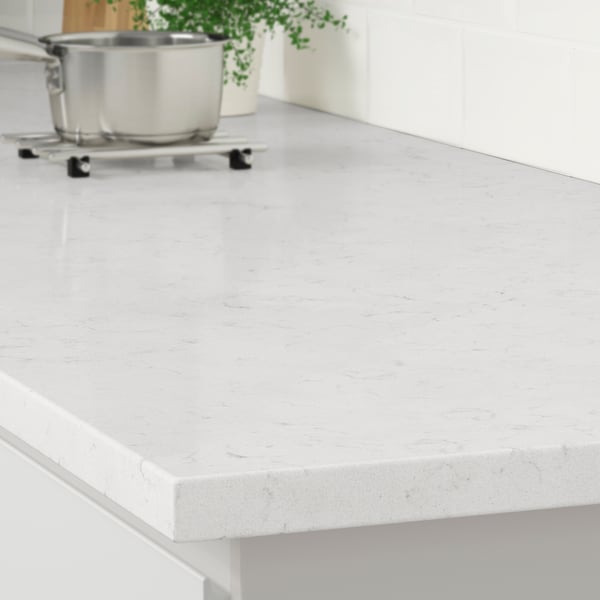 The corner of a LOCKEBO white marble effect countertop on a white kitchen cabinet with a stainless steel pot on a trivet.