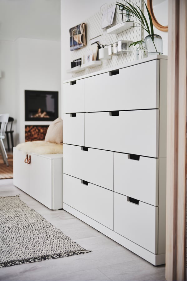 A white NORDLI chest of drawers standing against a white wall near the hallway area of an open floor-plan home interior.