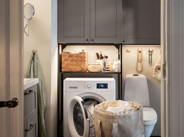 In a bathroom, a black ENHET laundry combination with one open shelf and closed storage with doors above the washing machine.