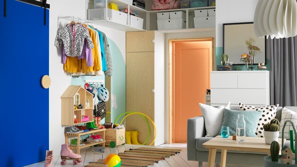 A hallway that opens into a living room. There is a PLATSA wardrobe on one side, with open shelving units above it.