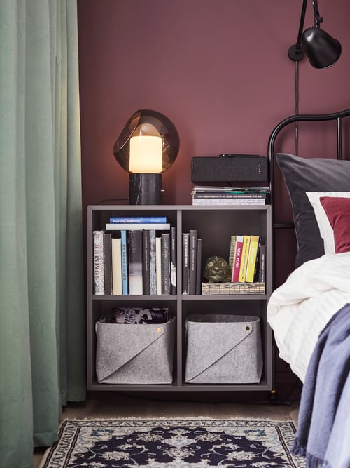 Bedroom with cabinet with four shelves, table lamp, speaker, bed frame, throw, duvet cover, rug, work lamp, cushion cover.
